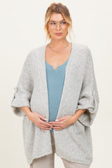 woman wearing a light gray maternity cardigan over a blue ribbed tank top and holding her baby bump