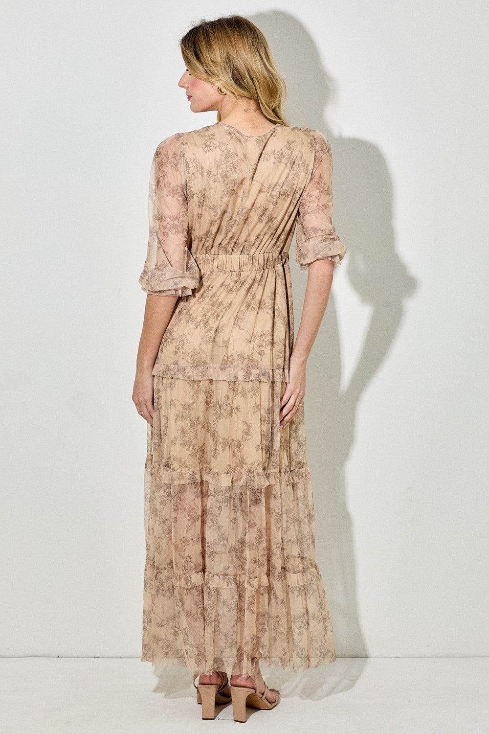 woman wearing a beige floral maxi dress with tiered ruffles and bell sleeves, viewed from the back