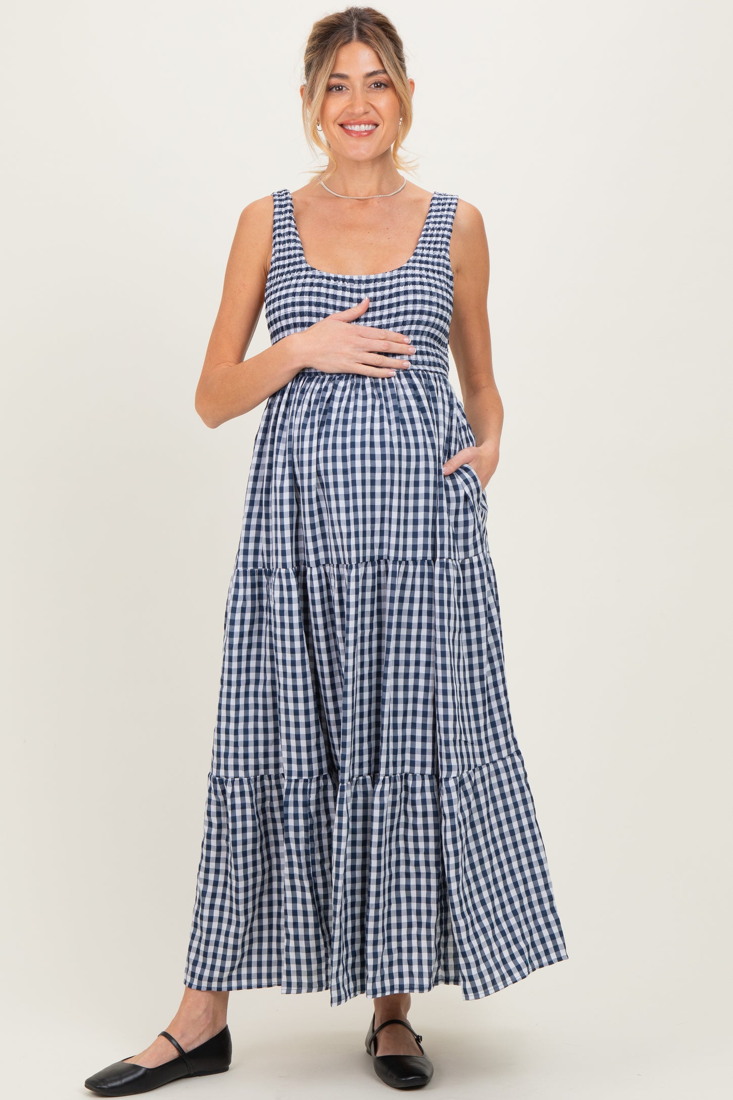 woman wearing a navy and white gingham maternity maxi dress, smiling and holding her baby bump