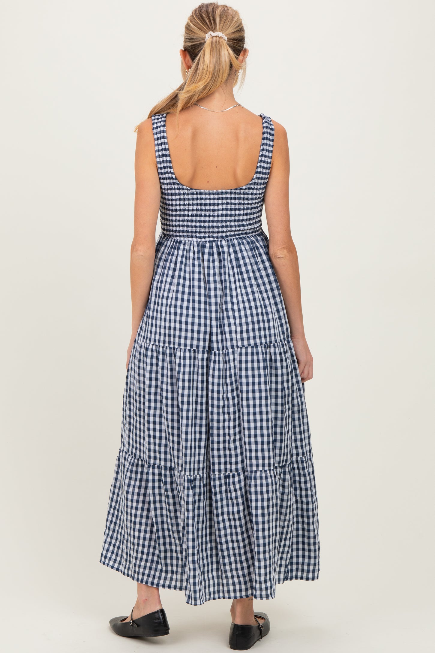 woman wearing a navy and white gingham maternity maxi dress with a tiered skirt and smocked back