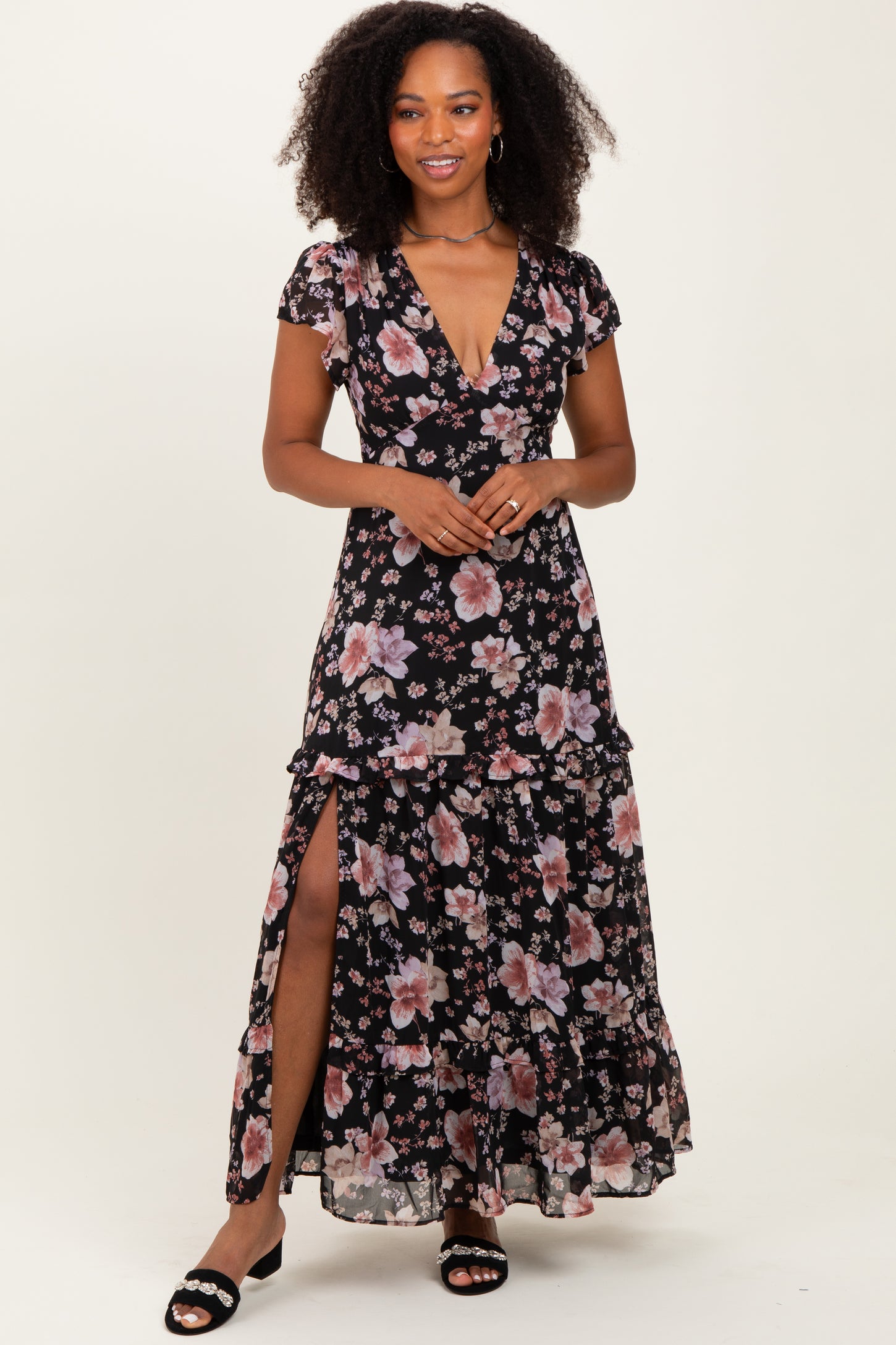 woman wearing a black floral maxi dress with ruffle details and a thigh-high slit