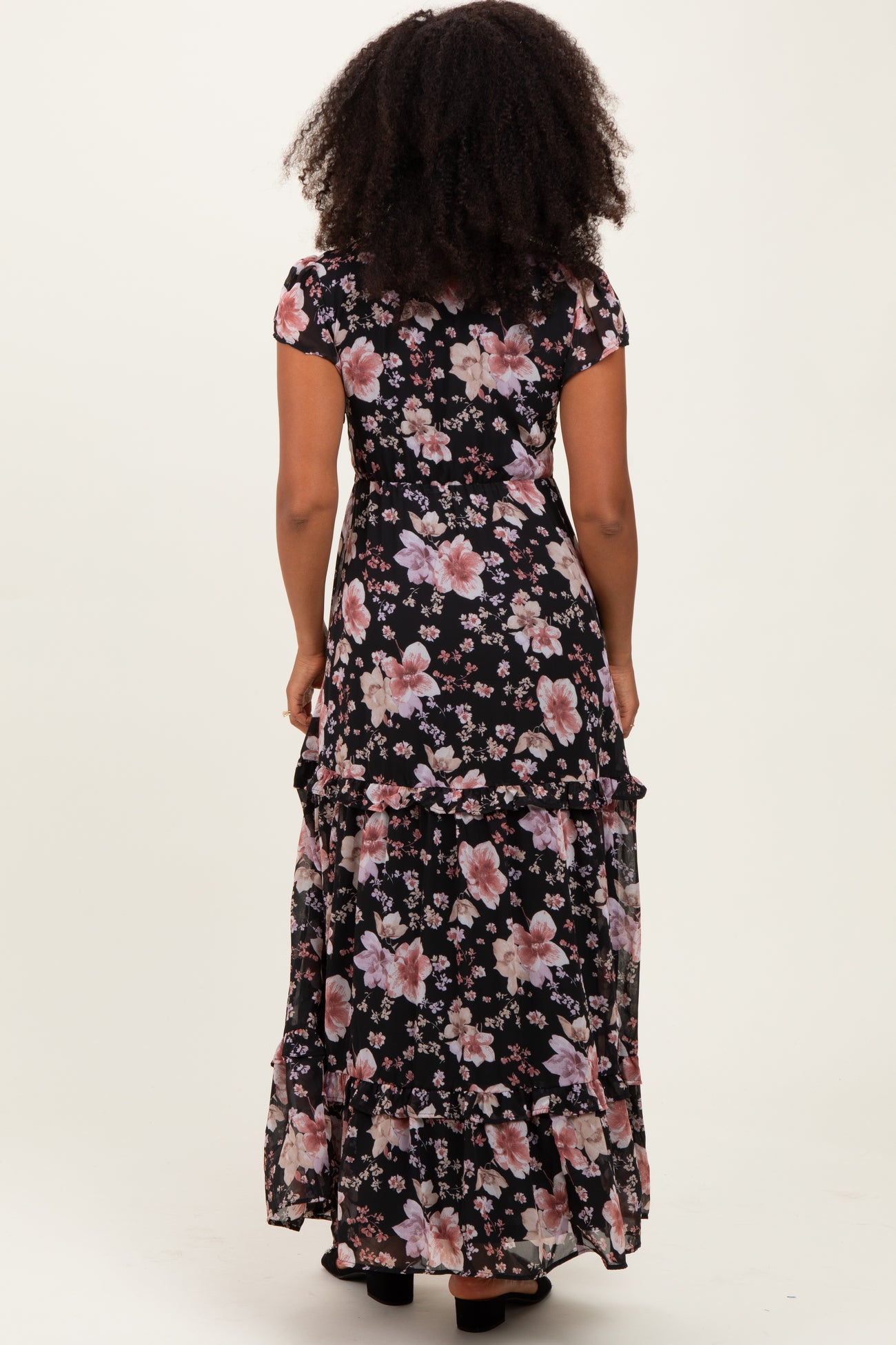 woman wearing a black floral maxi dress with short sleeves and ruffled hem, view from the back