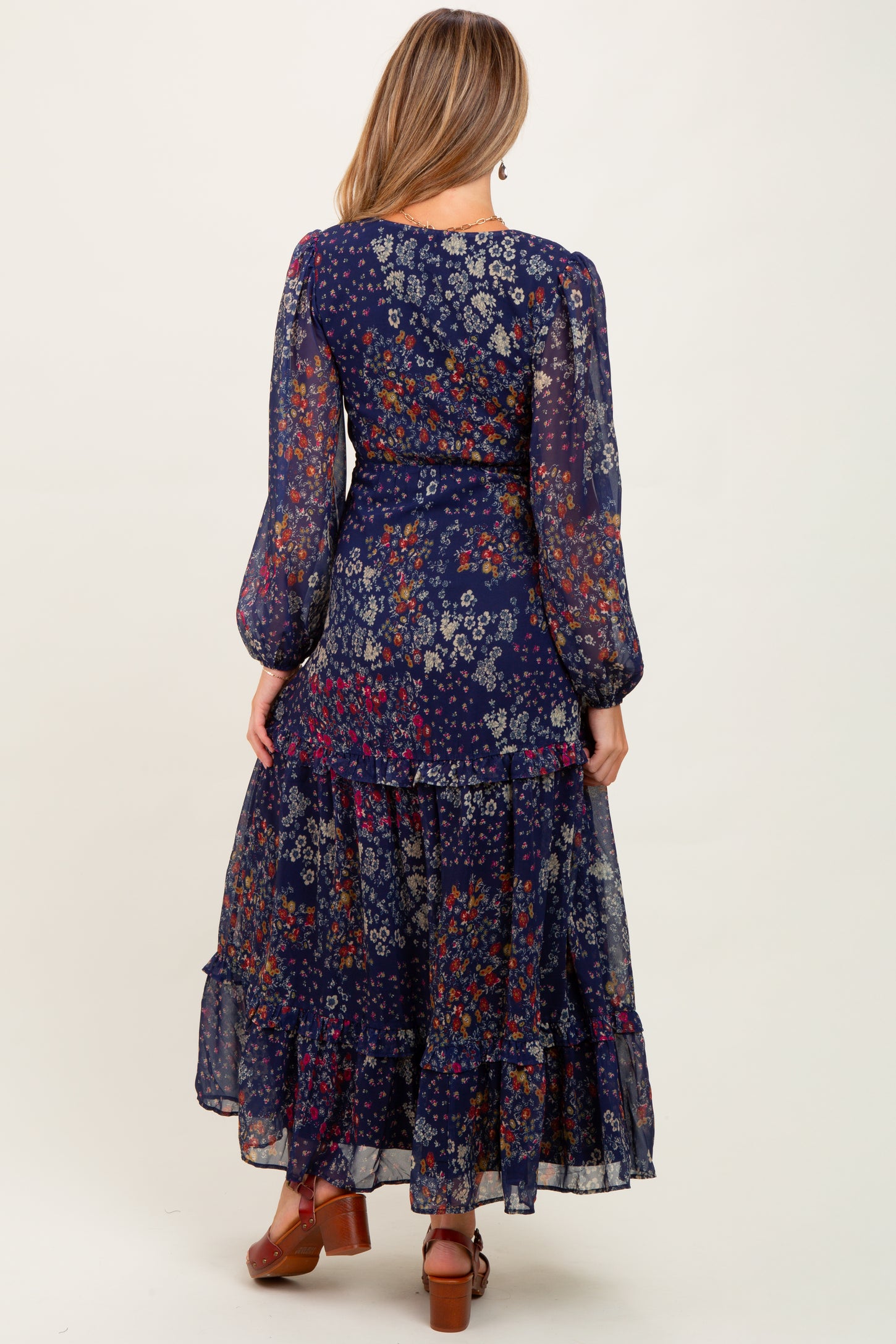 woman wearing a navy floral maternity dress with long sleeves and a tiered skirt, showing a baby bump