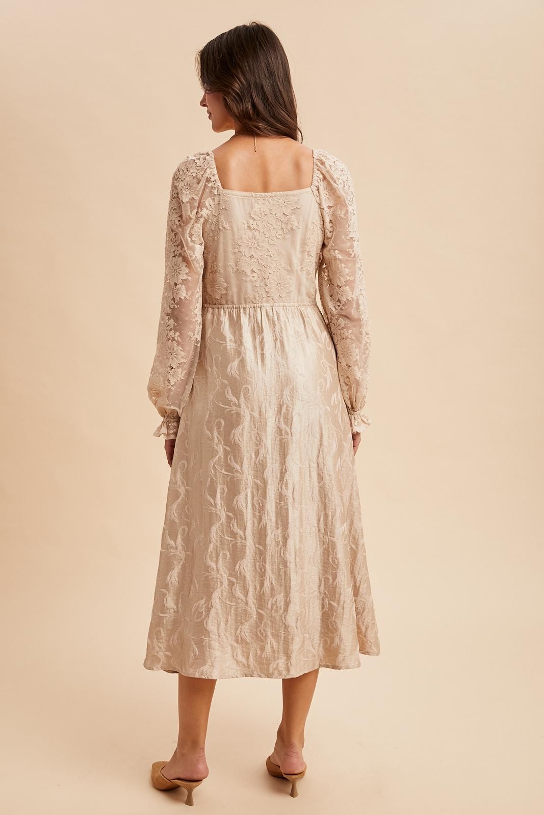 woman wearing a beige textured long sleeve dress with floral embroidery and a fitted waist, viewed from the back