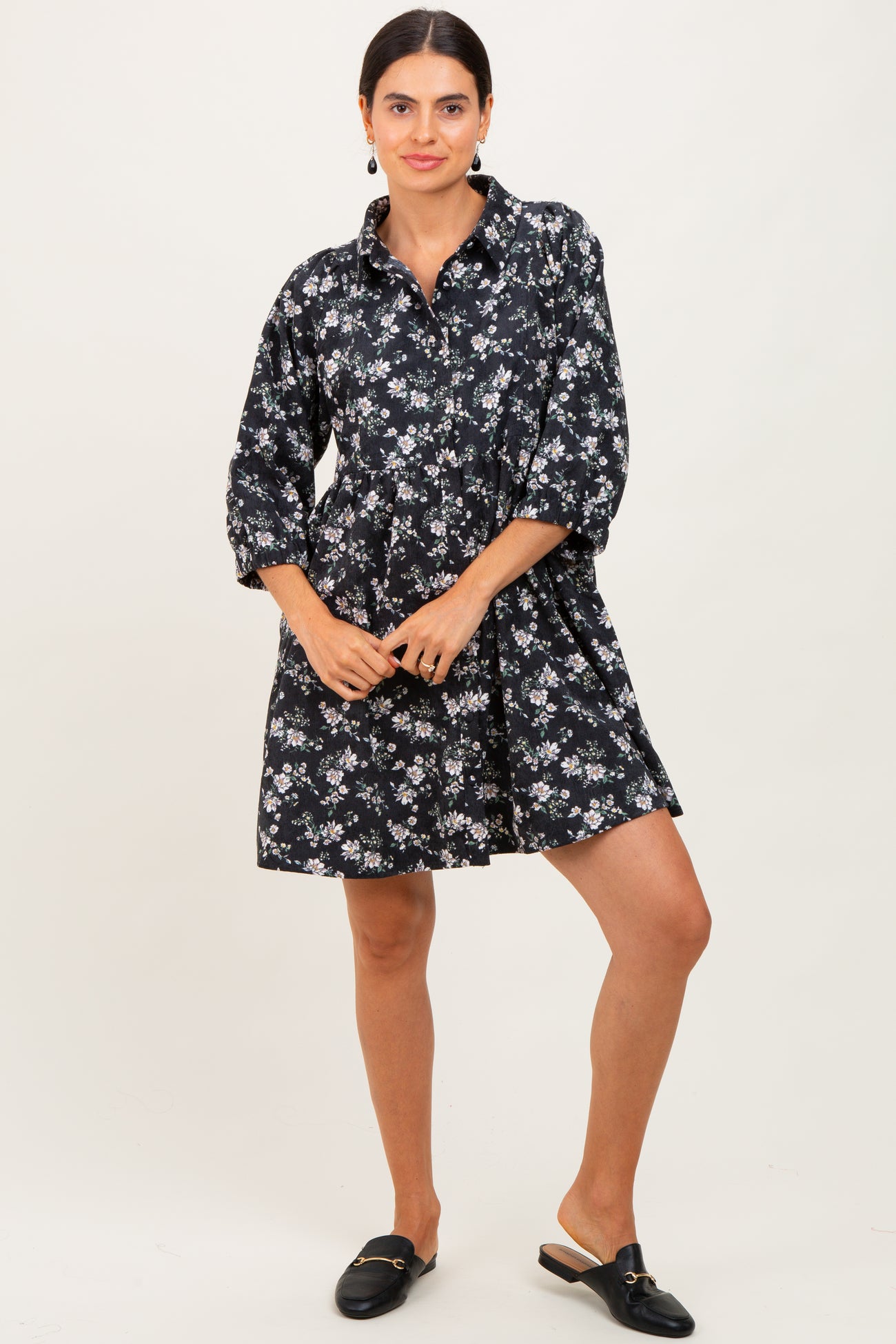 woman wearing a black floral shirt dress with three-quarter sleeves and a flared skirt, styled with black slip-on mules