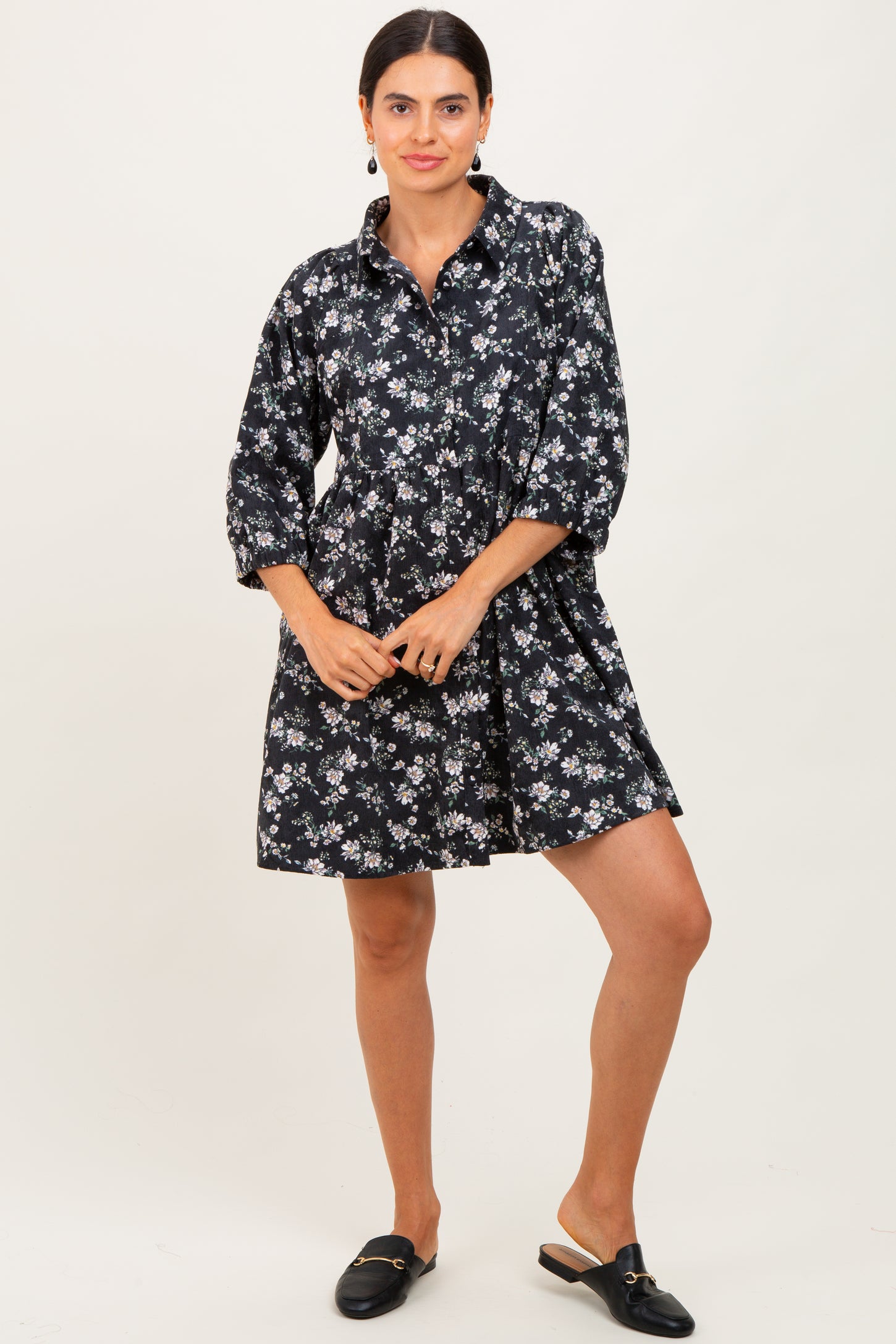 woman wearing a black floral shirt dress with three-quarter sleeves and a flared skirt, styled with black slip-on mules