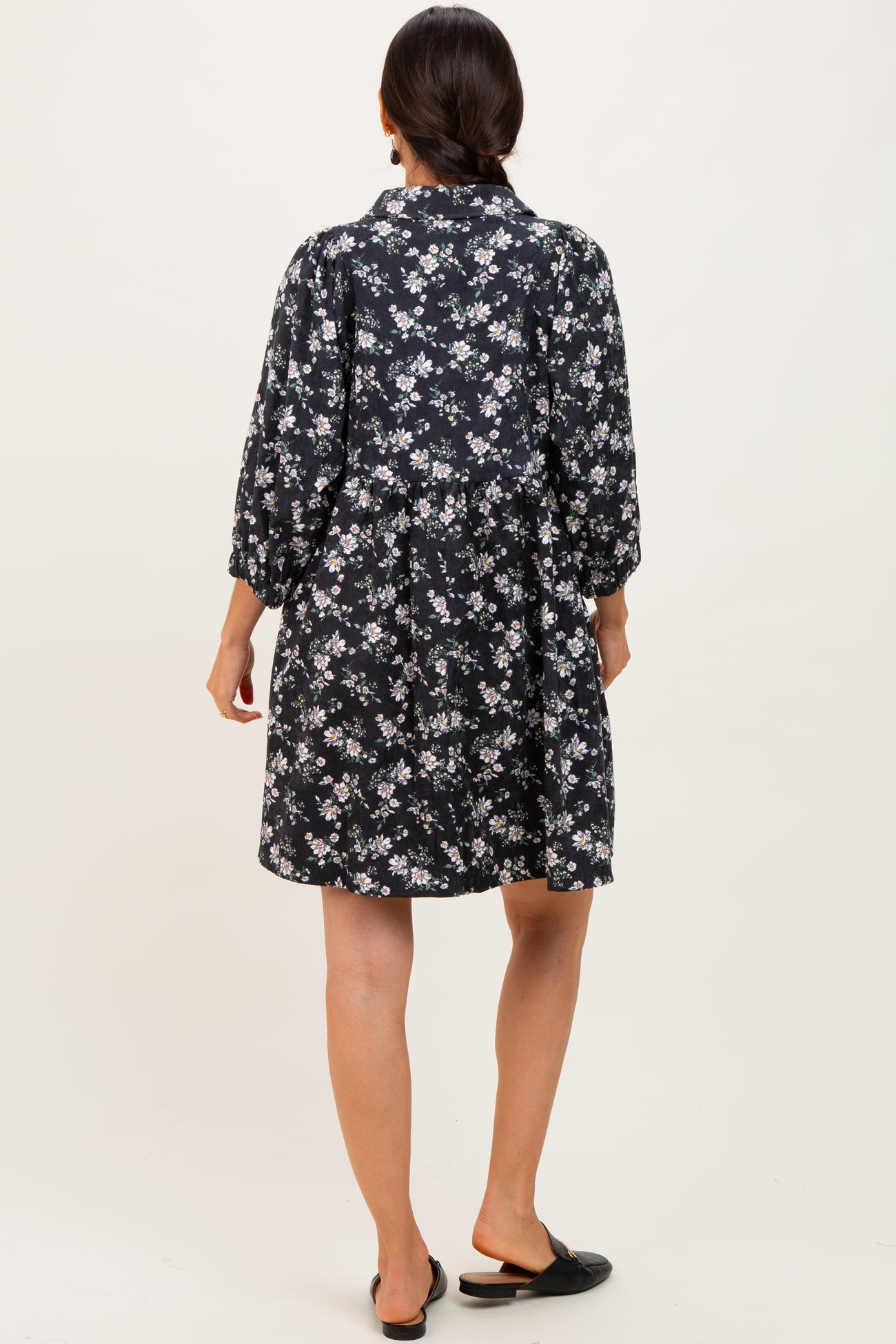 woman wearing a black floral print short dress with long sleeves and a loose fit, viewed from the back