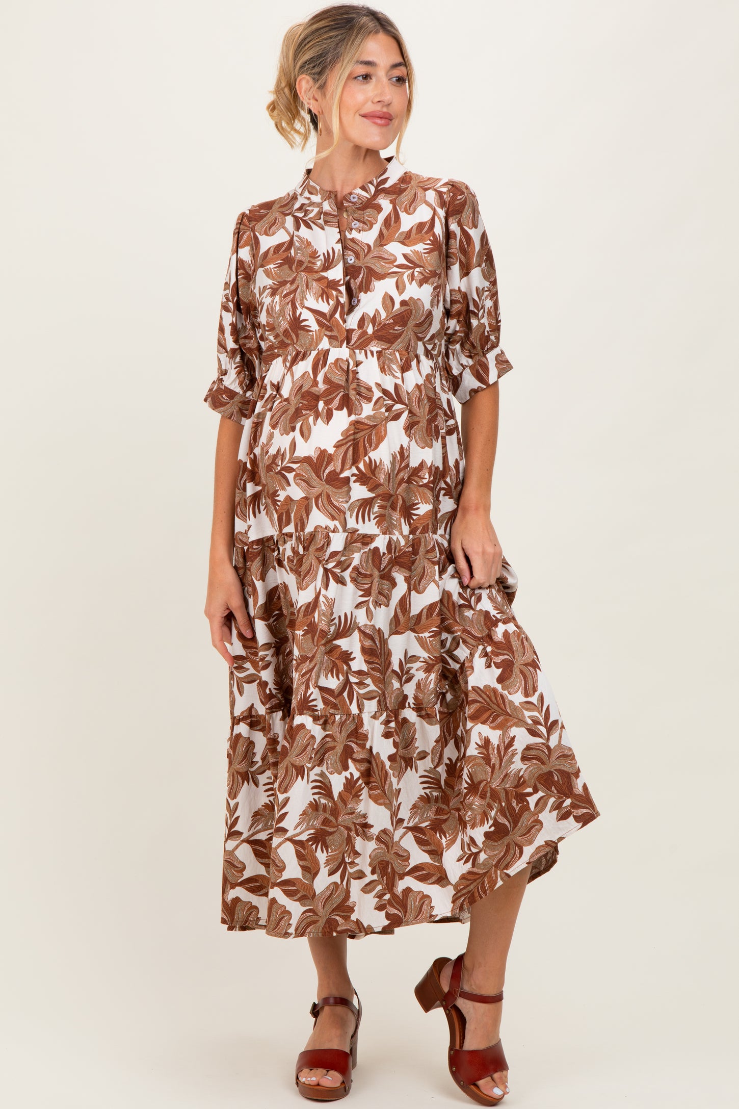 woman wearing a brown and white floral maxi maternity dress with short sleeves and a button-up front, showcasing her baby bump