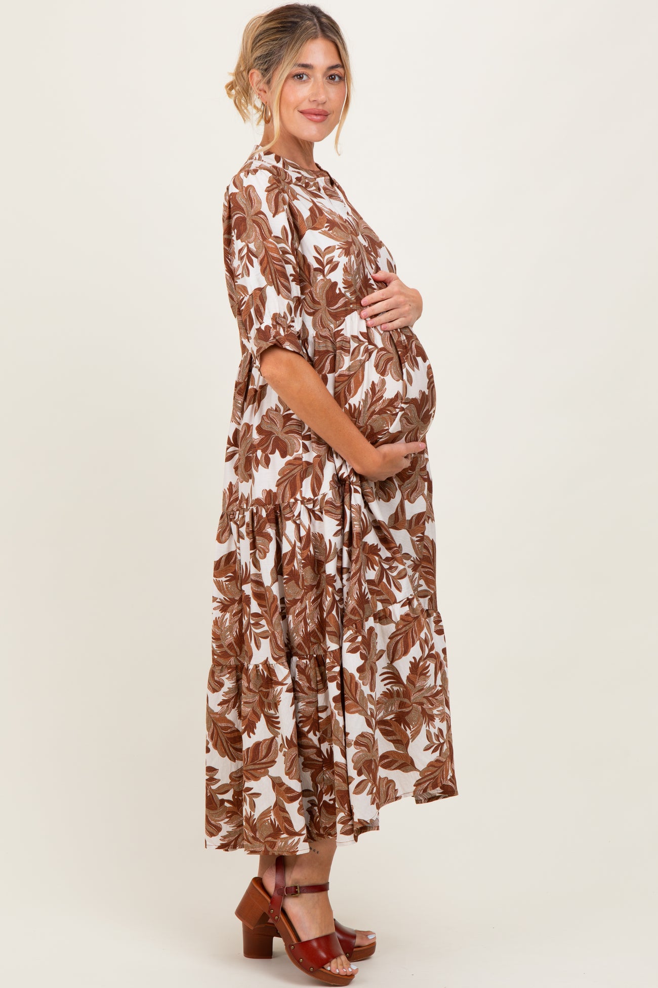 woman wearing a brown and white floral print maternity dress and holding her baby bump