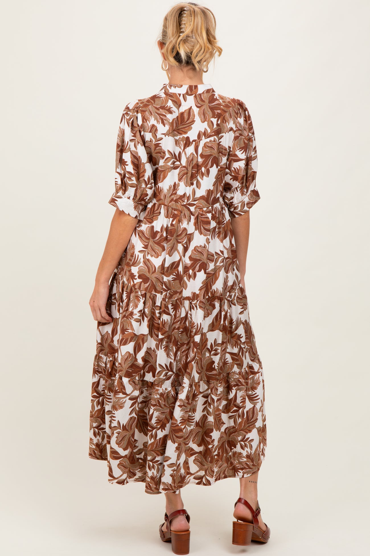 woman wearing a brown and white floral print maxi maternity dress with short sleeves and a tiered skirt