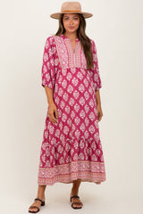 woman wearing a pink and white floral print maternity maxi dress with bell sleeves and a v-neckline, smiling and posing with a hat