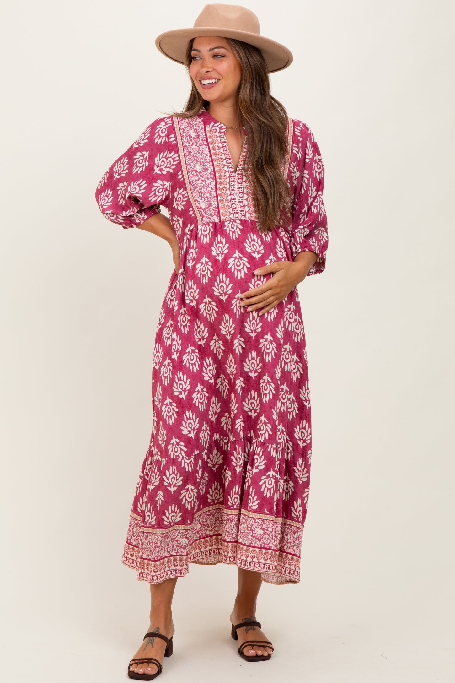 woman wearing a pink floral print maternity dress with a v-neck and balloon sleeves, lightly holding her baby bump