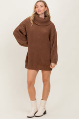 woman wearing a brown chunky knit sweater dress with a cowl neck and long sleeves, standing with one hand on her hip