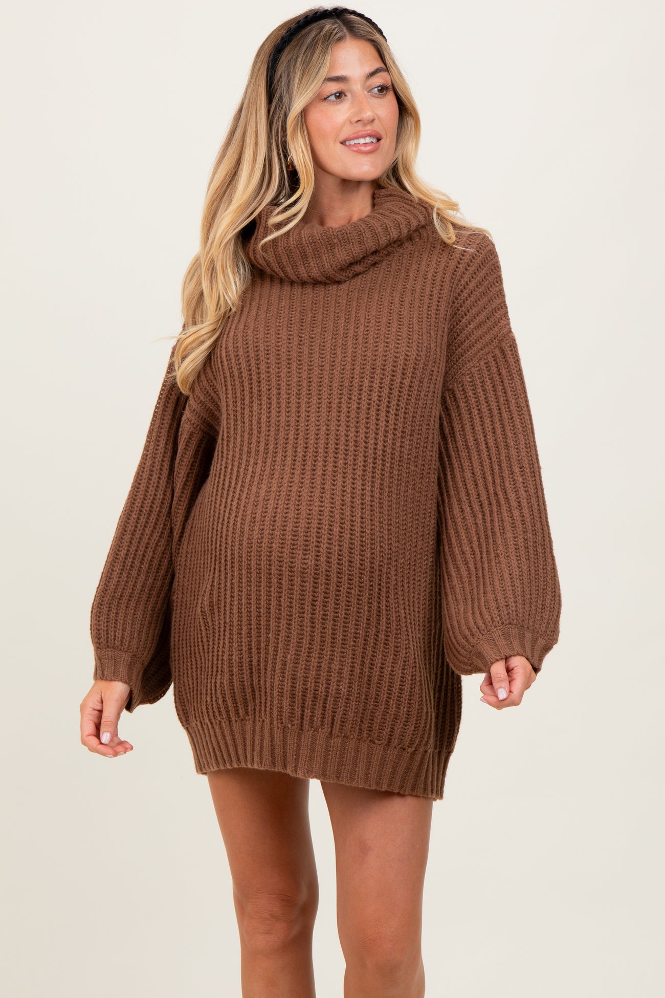 woman wearing a brown chunky knit maternity sweater with a cowl neck and oversized sleeves, showcasing a baby bump