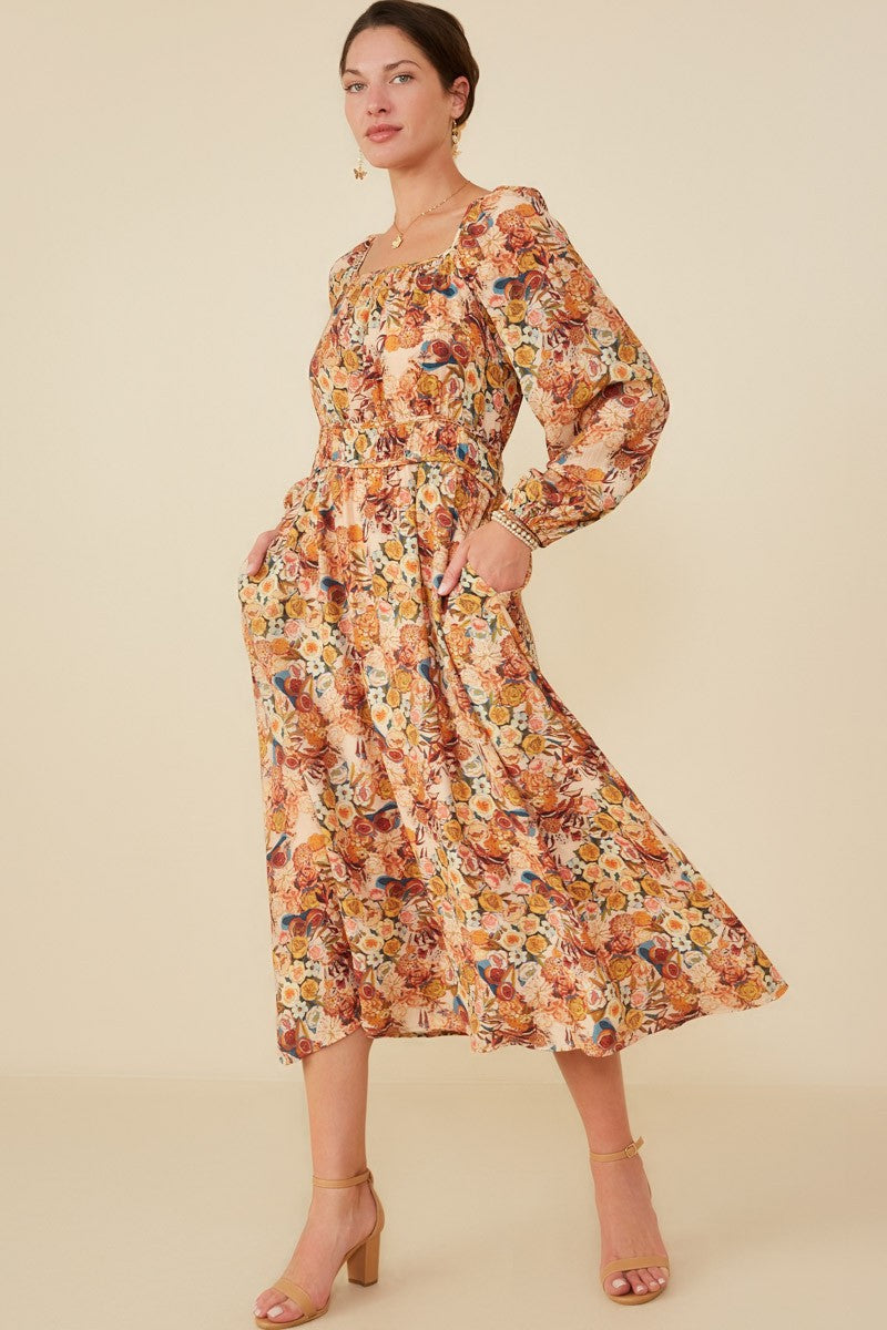 woman wearing a floral midi dress with long sleeves and pockets, styled with tan heeled sandals