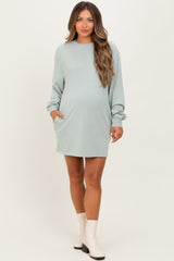 woman wearing a light green maternity sweatshirt dress with long sleeves and side pockets, showcasing her baby bump