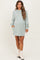 woman wearing a light green maternity sweatshirt dress with long sleeves and side pockets, showcasing her baby bump
