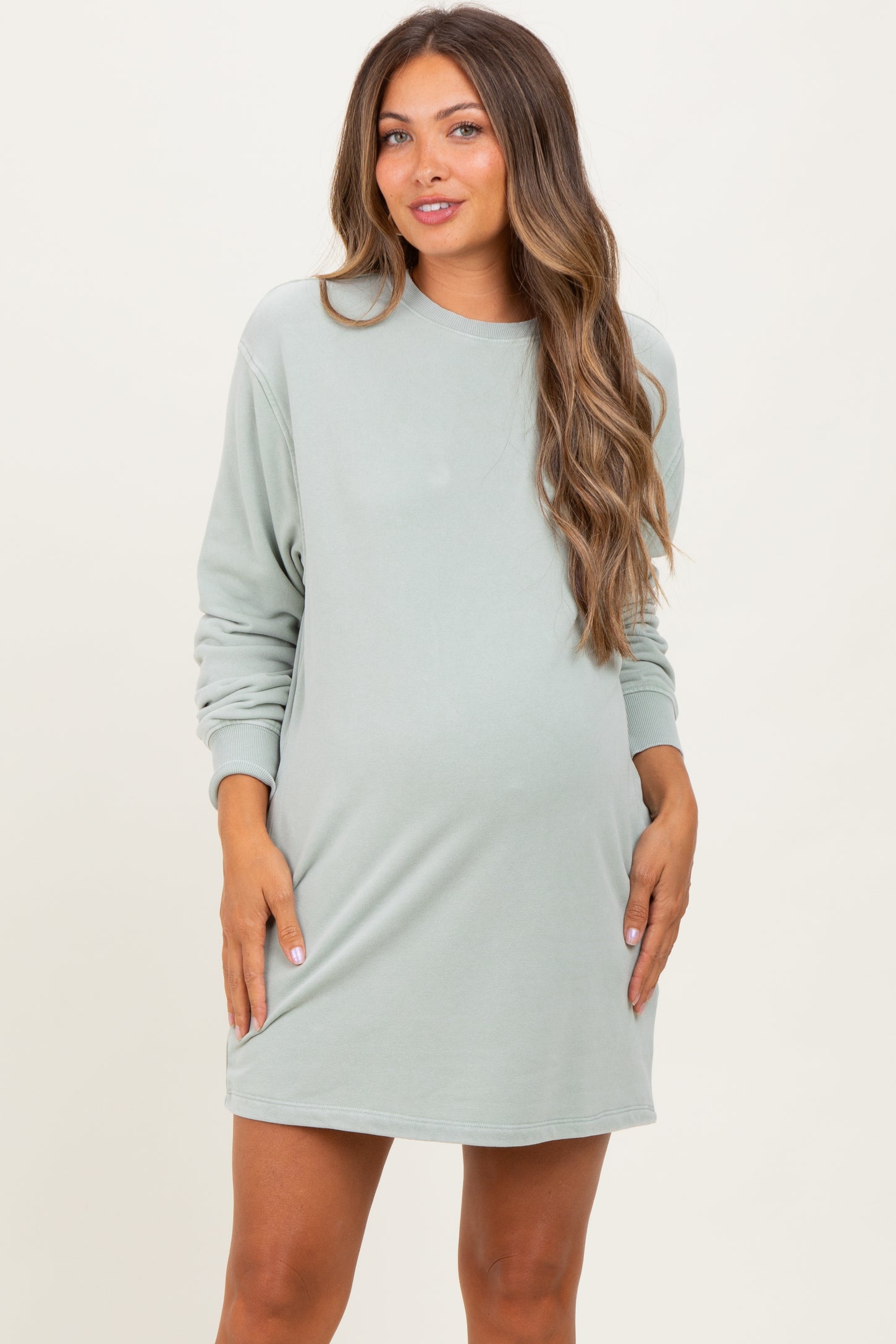woman wearing a light green long sleeve maternity dress and showing her baby bump