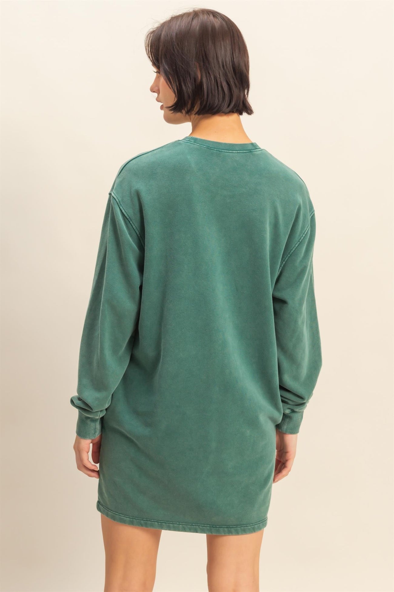 woman wearing a green oversized sweatshirt dress with long sleeves and a relaxed fit, seen from the back