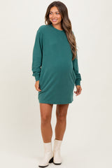 woman wearing a dark green maternity sweatshirt dress with long sleeves and a visible baby bump