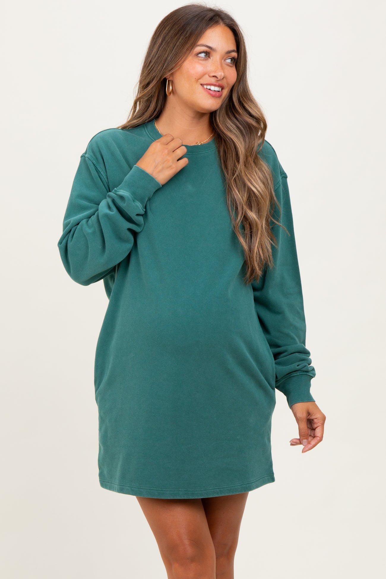 woman wearing a green oversized casual maternity dress with long sleeves and a smile, highlighting her baby bump