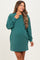 woman wearing a green oversized casual maternity dress with long sleeves and a smile, highlighting her baby bump