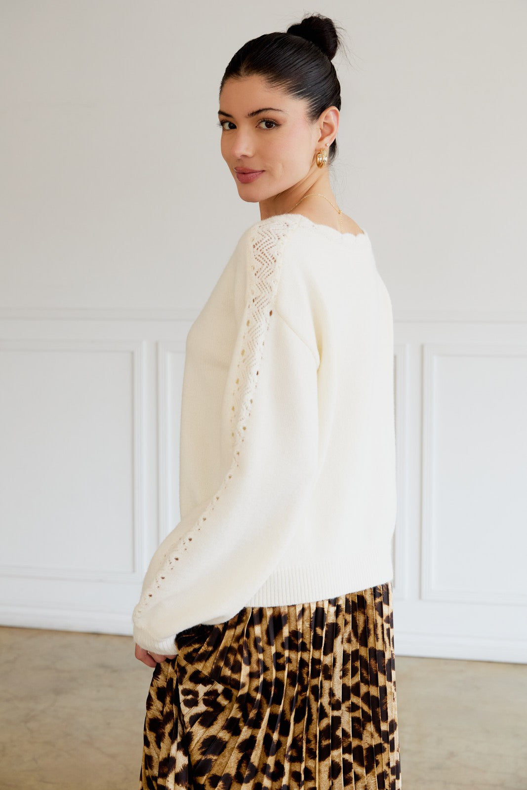 woman wearing a cream long sleeve sweater with lace detail on the sleeves and a printed pleated skirt