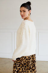 woman wearing a cream long sleeve sweater with lace detail on the sleeves and a printed pleated skirt