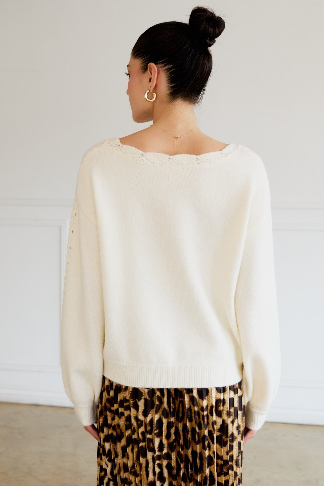 woman wearing a cream-colored oversized sweater with a lace detail on the back and paired with a leopard print skirt