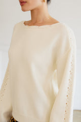 woman wearing a cream-colored knitted sweater with a wide neckline and intricate detailing on the sleeves
