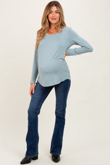 woman wearing a light blue long sleeve maternity top and showing her baby bump, paired with flared jeans