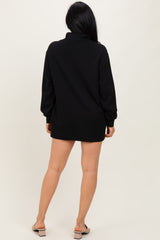 woman wearing a black oversized pullover dress with long sleeves and a high collar, shown from the back