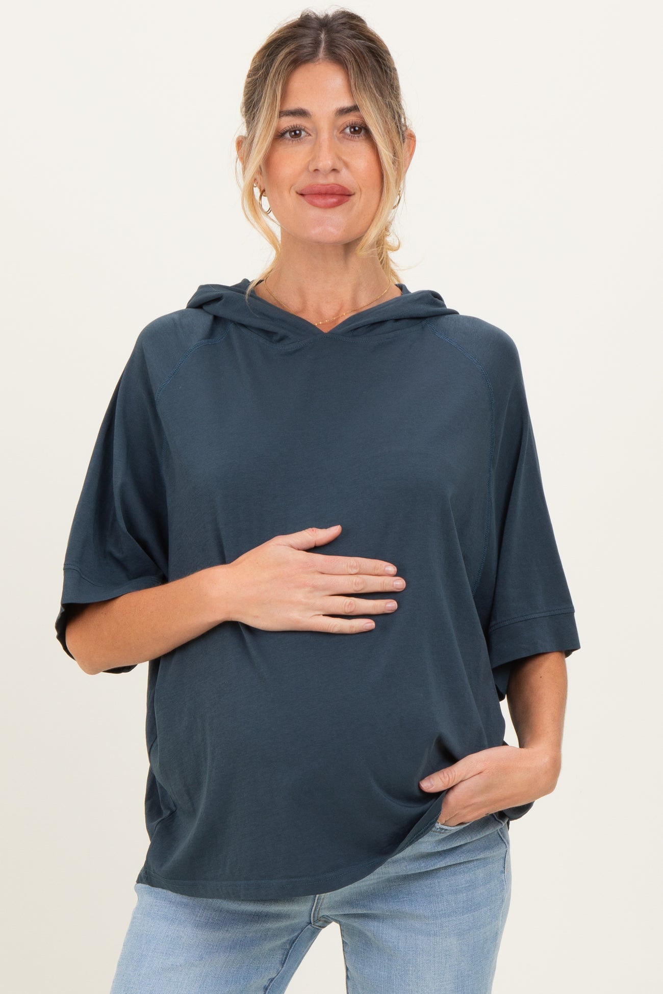 woman wearing a dark teal maternity hoodie and holding her baby bump