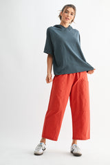 woman wearing a teal oversized hoodie and bright orange wide-leg pants, standing casually against a white background