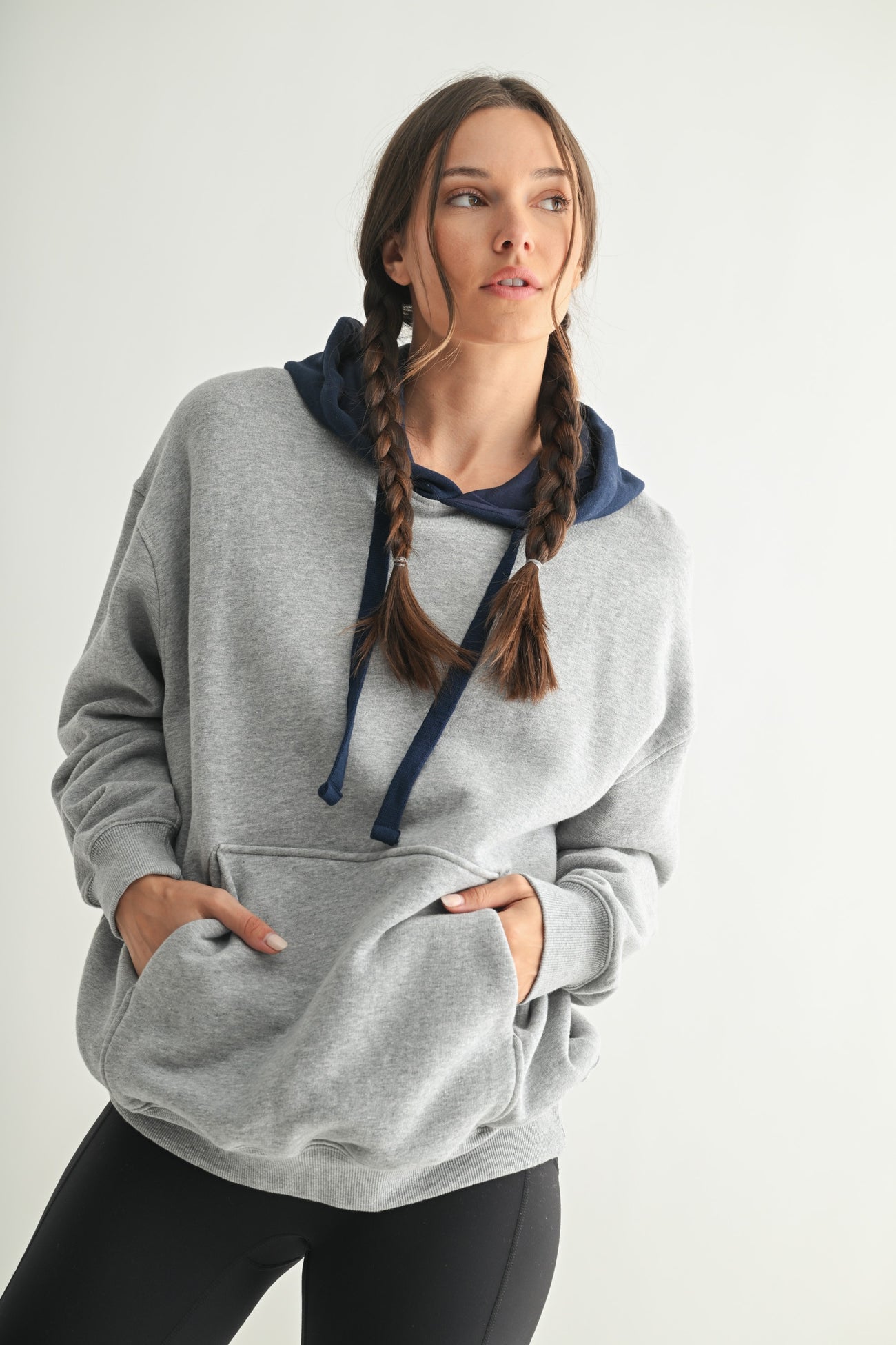 woman wearing a gray oversized hoodie with a navy blue hood and pockets, styled with black leggings