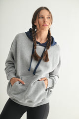 woman wearing a gray oversized hoodie with a navy blue hood and pockets, styled with black leggings