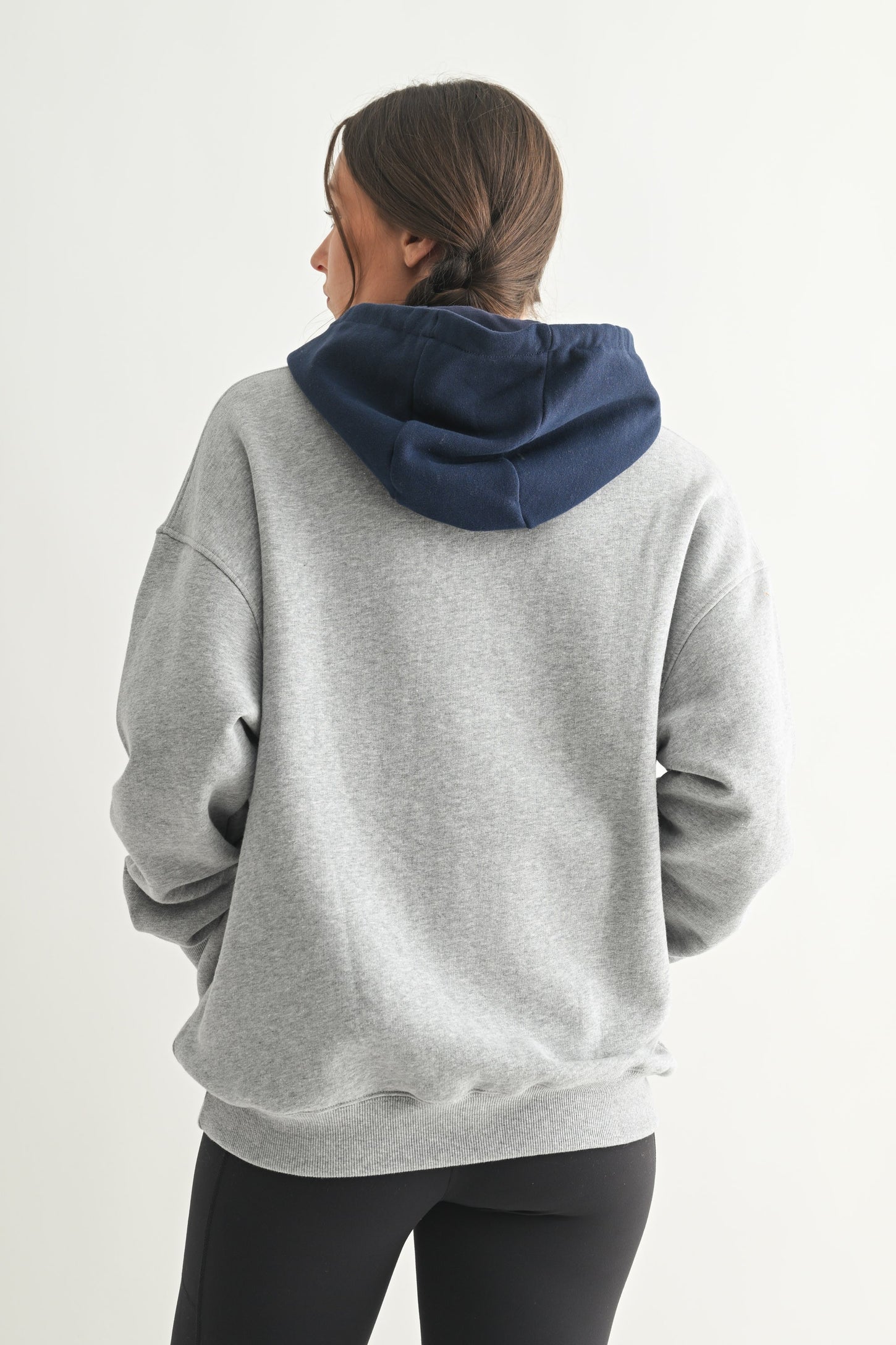 woman wearing a gray oversized hoodie with a navy blue hood and a relaxed fit, seen from the back