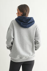 woman wearing a gray oversized hoodie with a navy blue hood and a relaxed fit, seen from the back
