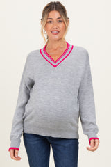 woman wearing a gray maternity sweater with a pink v-neck trim and a visible baby bump