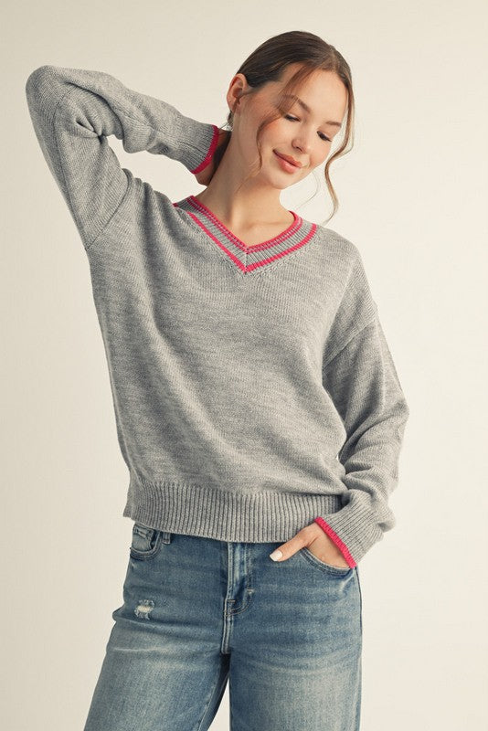 woman wearing a gray v-neck sweater with pink trim and styled with light blue jeans