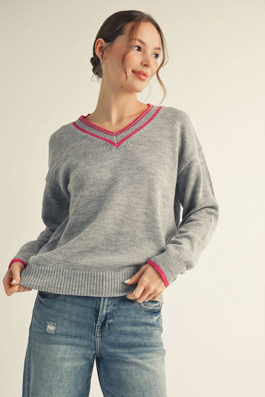 woman wearing a gray v-neck sweater with pink trim and distressed blue jeans