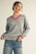 woman wearing a gray v-neck sweater with pink trim and distressed blue jeans