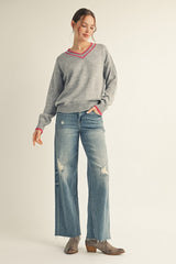 woman wearing a gray v-neck sweater with pink trim and distressed wide-leg jeans, paired with ankle boots