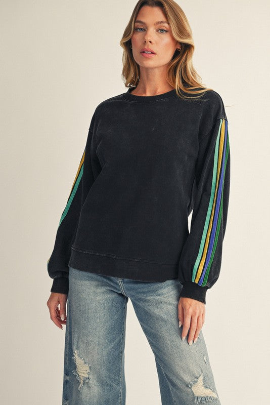 woman wearing a black sweatshirt with colorful striped sleeves and distressed light blue jeans