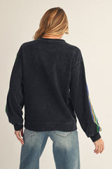 woman wearing a black oversized sweatshirt with colorful striped sleeve details and blue jeans, seen from the back
