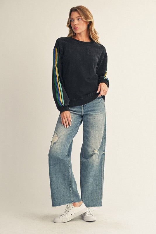woman wearing a black long sleeve top with colorful stripes on the sleeves and distressed wide leg jeans