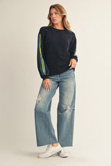 woman wearing a black long sleeve top with colorful stripes on the sleeves and distressed wide leg jeans