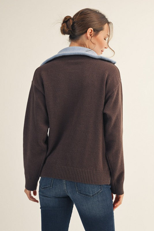woman wearing a brown sweater with a blue collar, seen from the back, paired with blue jeans