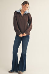 woman wearing a brown zip-up sweater with a light blue collar and flared blue jeans