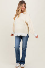 woman wearing a cream and white striped maternity sweater with balloon sleeves and blue flared jeans, showing her baby bump